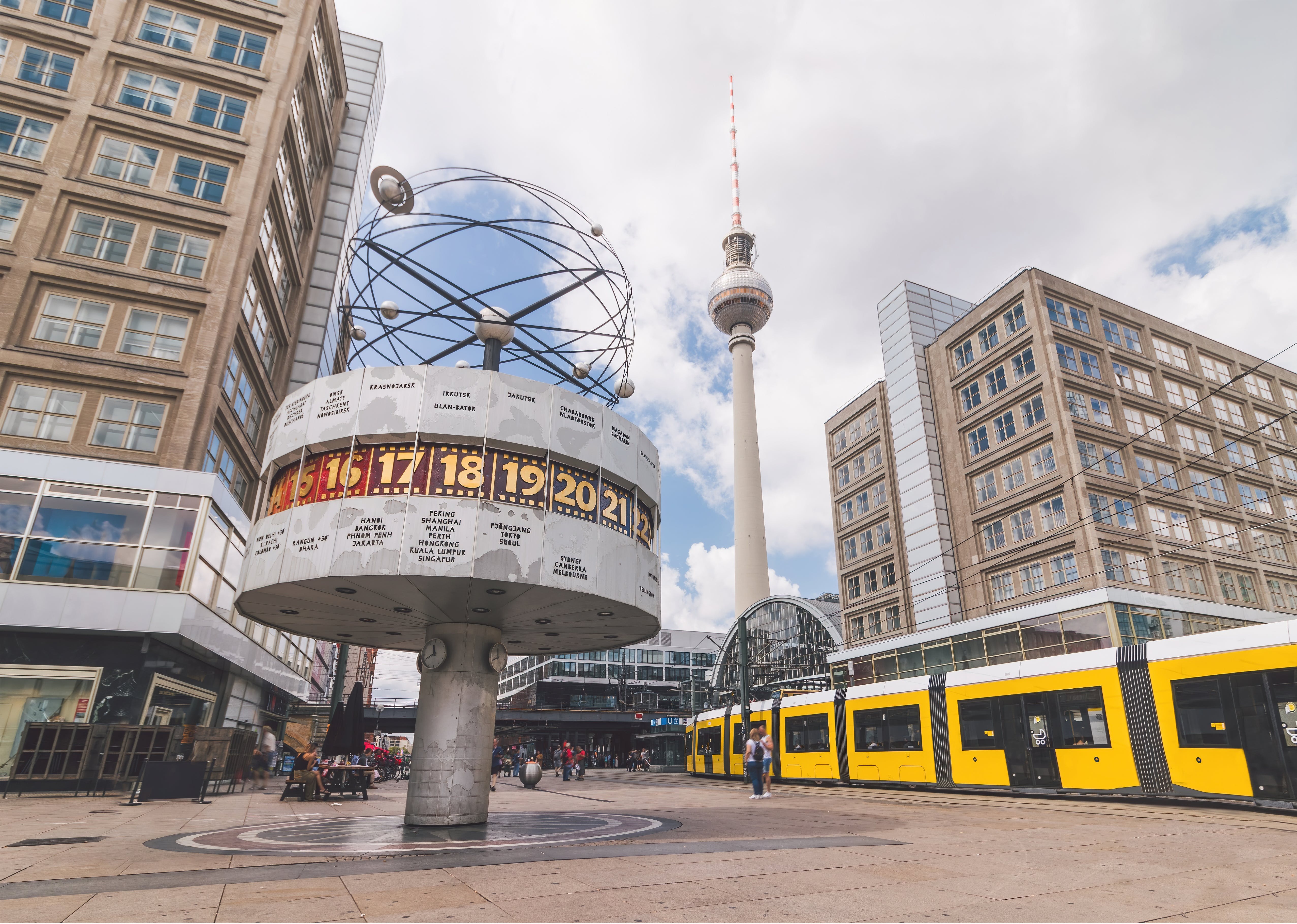 image is of the world clock in Alexanderplatz with a yellow tram on the right-hand side of the image