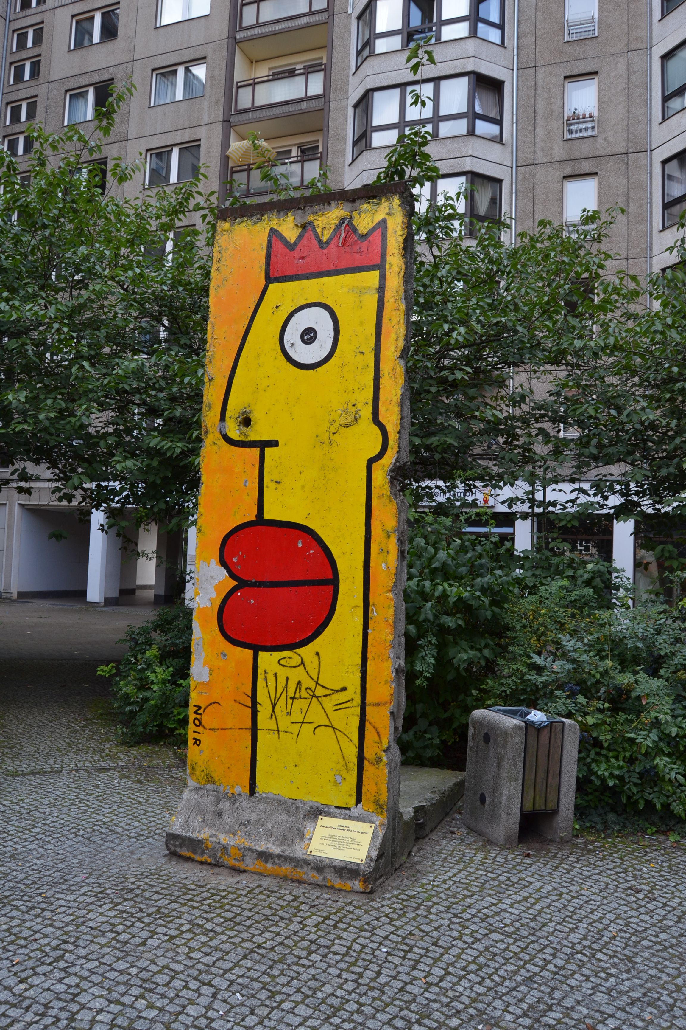 panel of the Berlin wall that has a cartoonish yellow face with red hair and lips